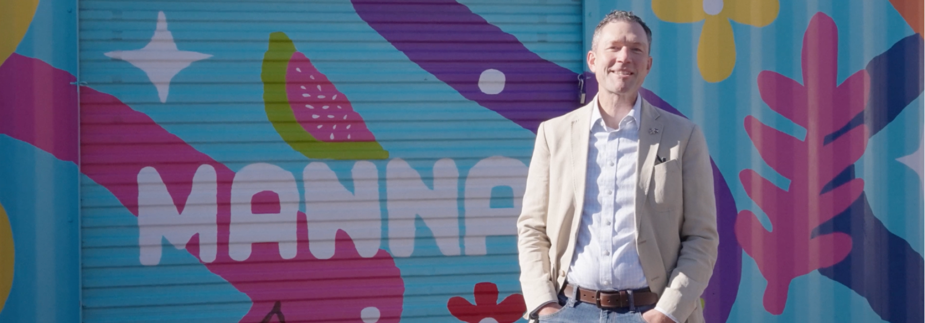 Chris in front of colorful Manna mural 