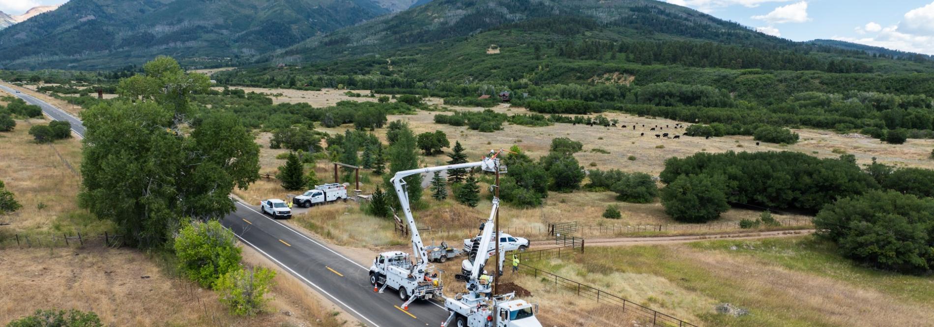LPEA bucket trucks on a rural road with mountains in the background