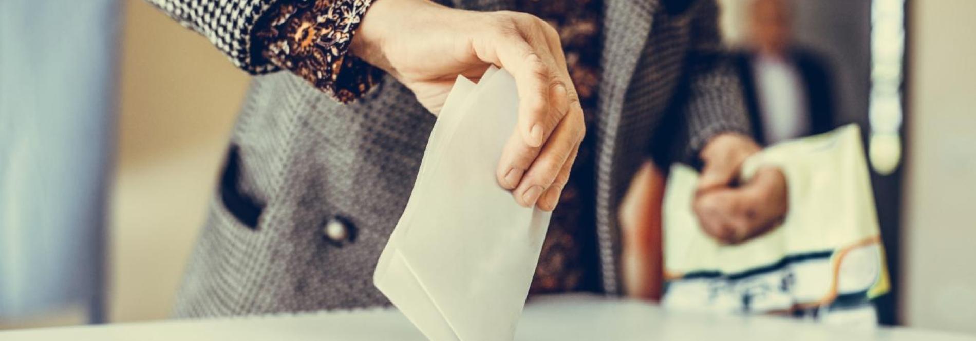 a hand placing a ballot in a ballot box