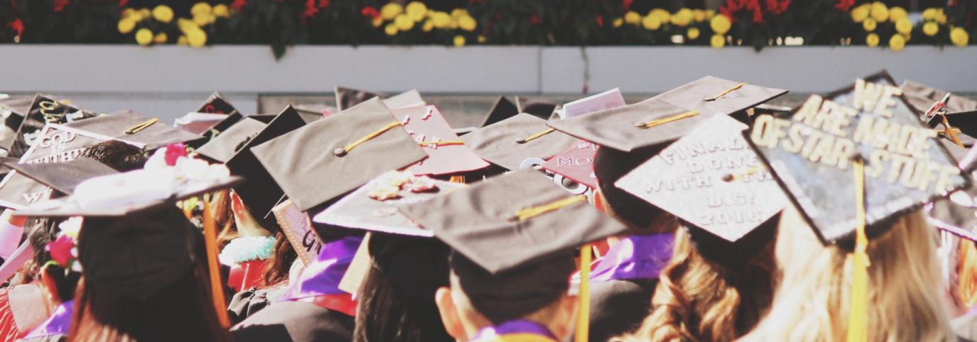 Graduates wearing graduation caps looking towards a stage